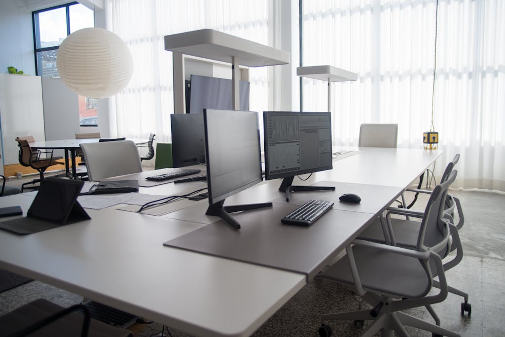 Spacious modern office featuring multiple computers, chairs, and collaborative workstations in natural light.